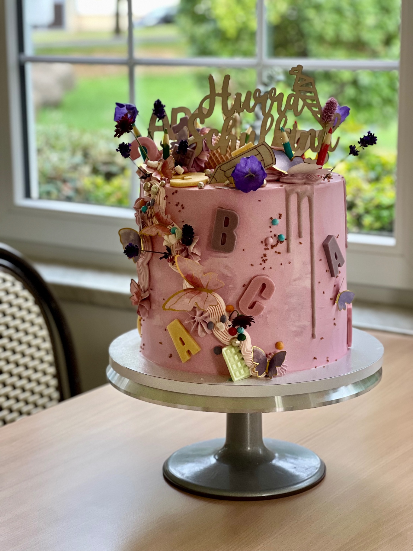 Hurra Schulkind — ABC — Rosa mit Schokoladen-Buchstaben, Schmetterlingen und Zuckerstiften.. Motivtorte aus Lauras Tortenmanufaktur, Meitzendorf bei Magdeburg.