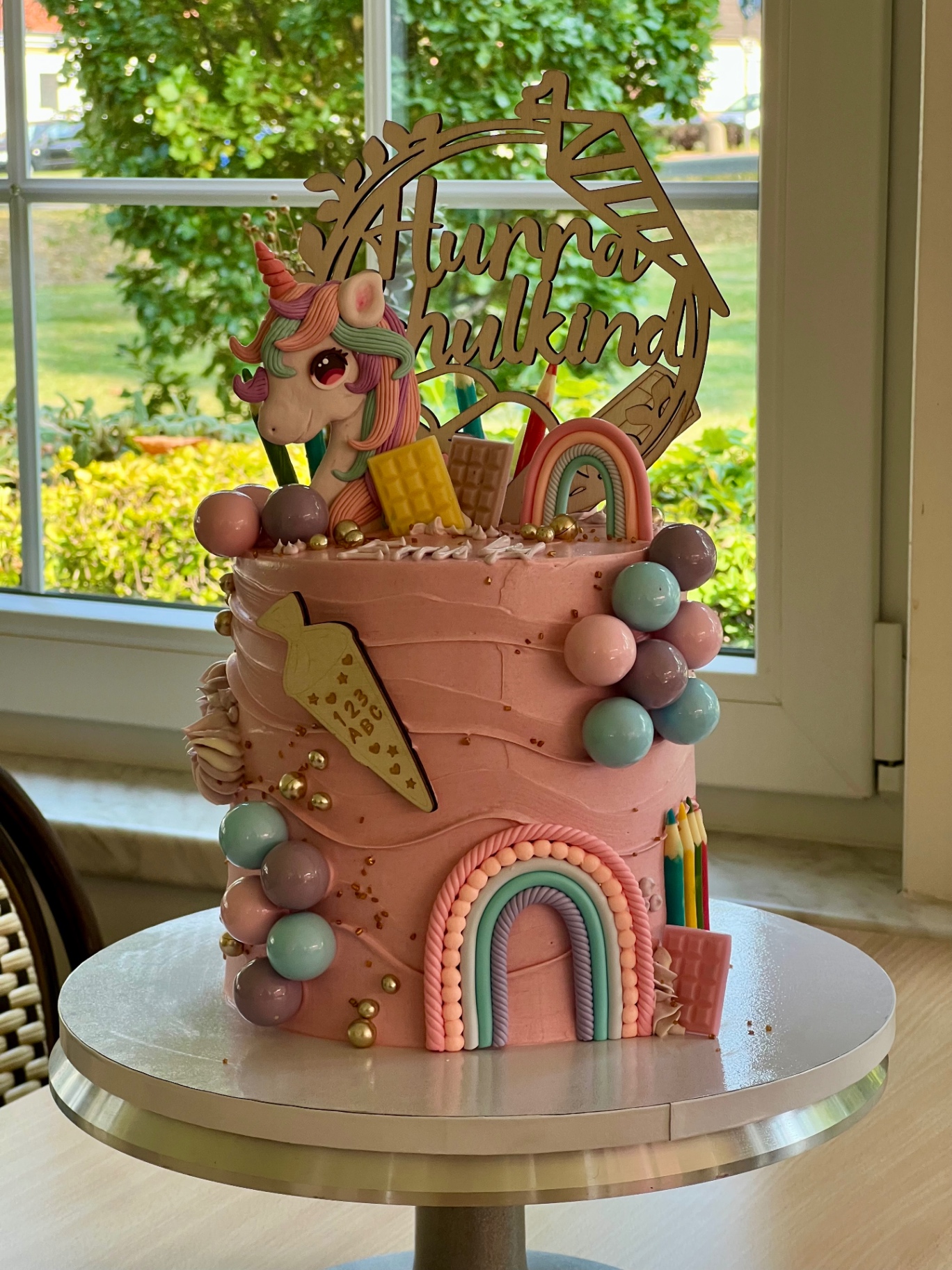 Hurra Schulkind — Einhorn — Rosa mit Einhorn-Topper, Regenbogen und pastellfarbenen Choco-Balls.. Motivtorte aus Lauras Tortenmanufaktur, Meitzendorf bei Magdeburg.