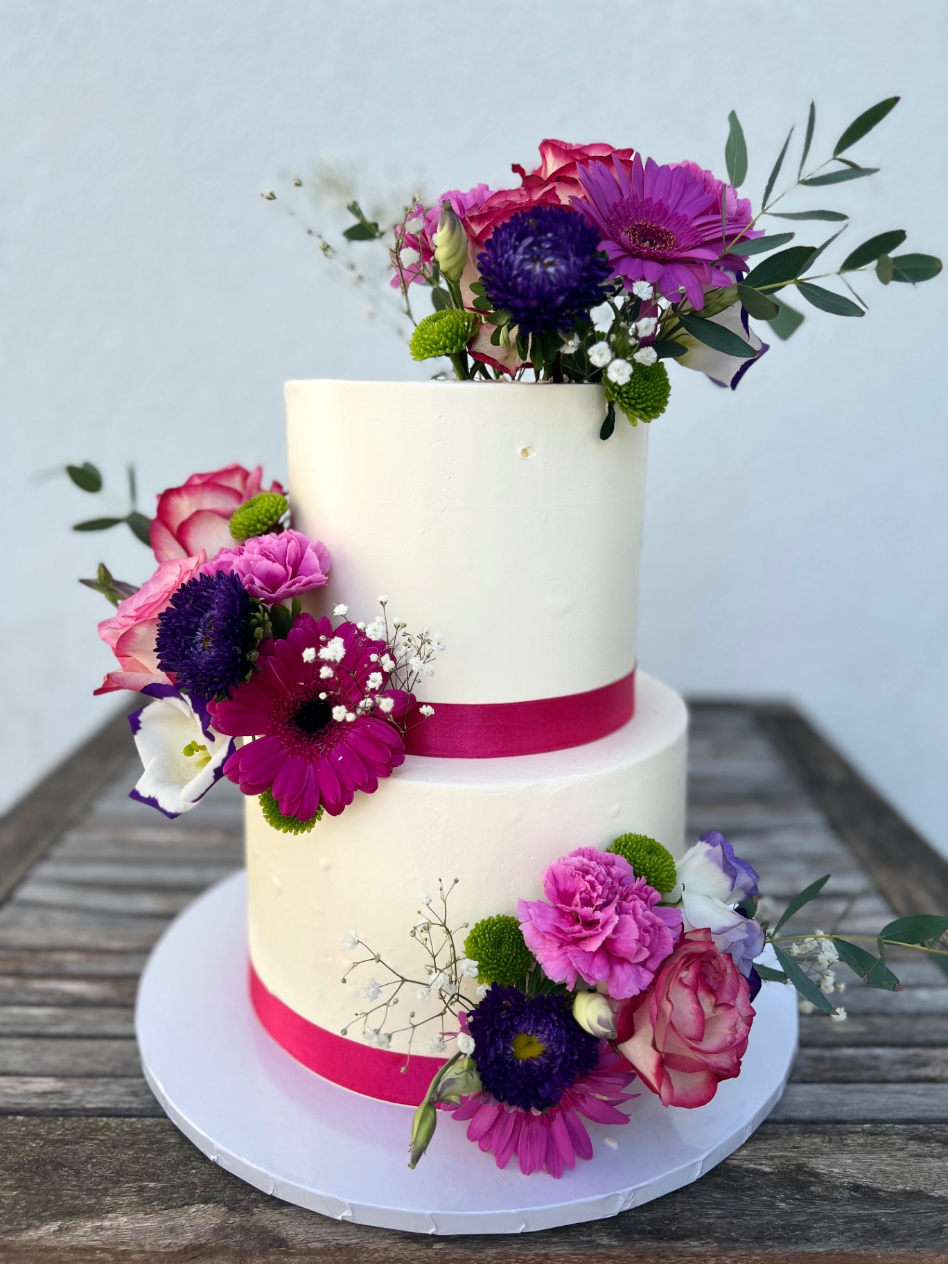 Sommerblüten — Zweistöckig in Weiß mit pinkfarbenem Band und opulenten Sommerblumen.. Hochzeitstorte aus Lauras Tortenmanufaktur, Meitzendorf bei Magdeburg.